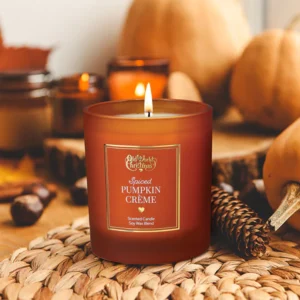 Hand-poured Pumpkin Cream Candle surrounded by pumpkins, cinnamon sticks, and fall leaves.