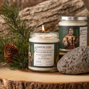 Hand-poured Campfire Candle surrounded by wood logs and glowing embers.